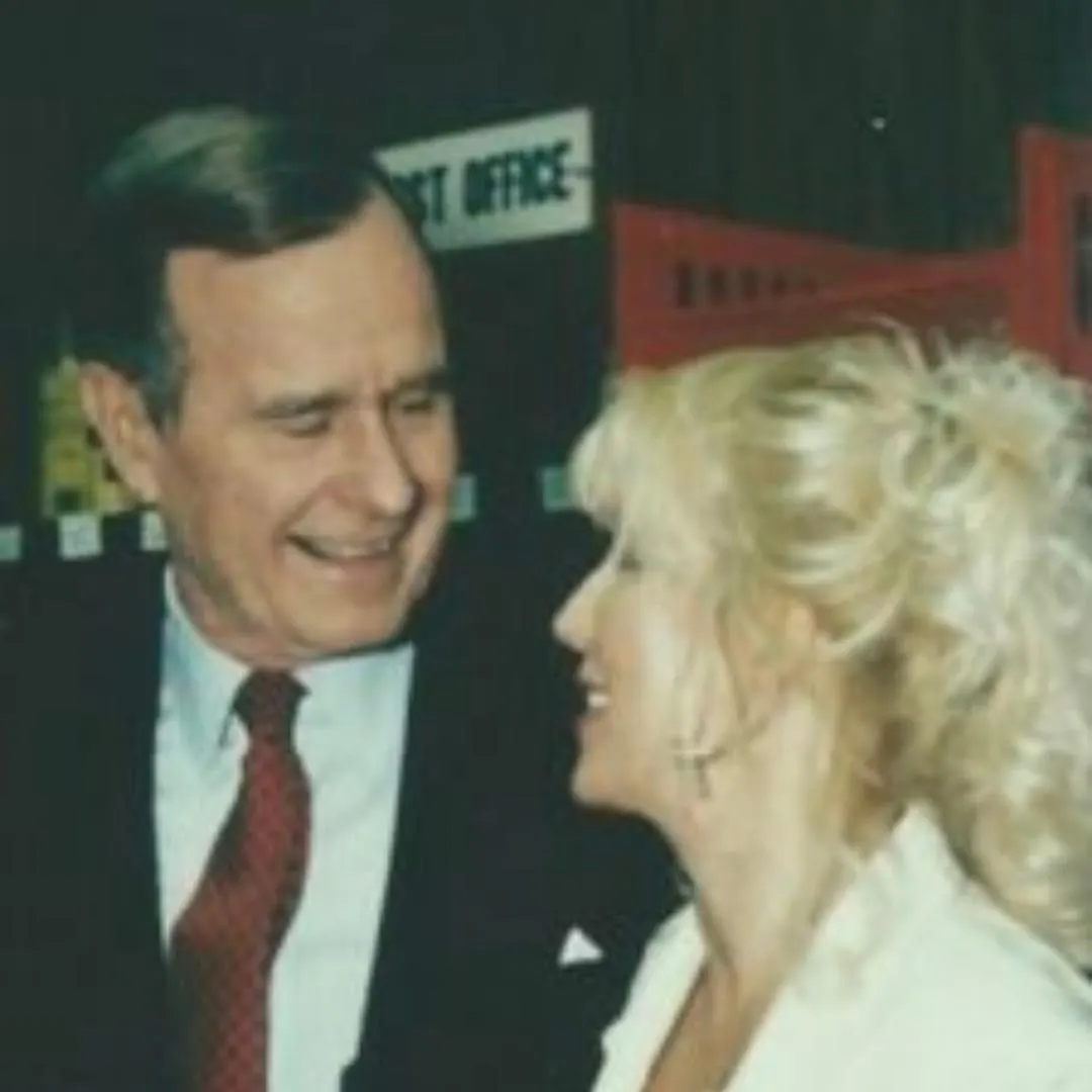 A woman with blonde hair smiles while talking to a man in a suit and red tie in an indoor setting. This image captures a moment of connection, reflecting themes of nonprofit leadership and advocacy related to Linda Smith.| Linda’s Life – Linda Smith