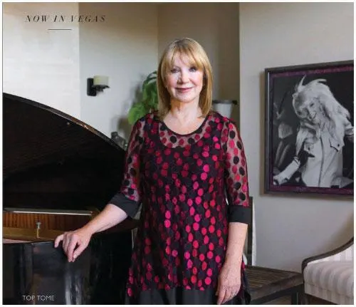 A woman stands beside a grand piano, wearing a red and black patterned blouse, with a portrait in the background. The setting is elegant and calm, reflecting her role as a motivational speaker and disability advocate.| Linda’s Life – Linda Smith