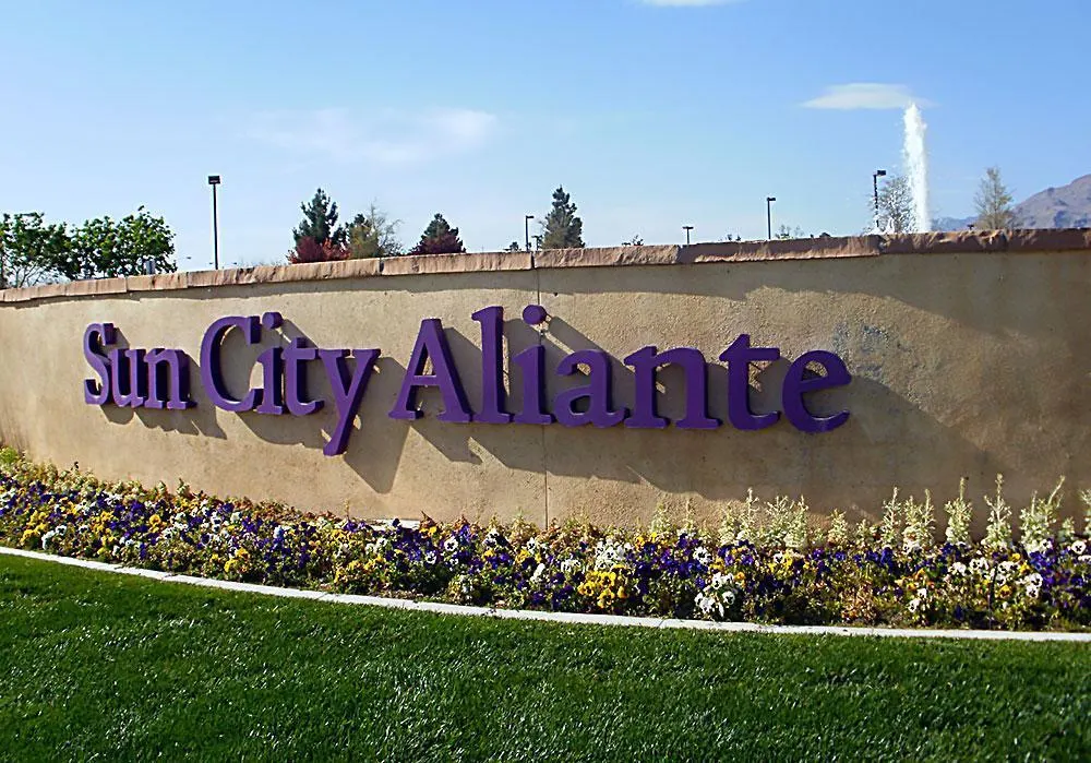 A stone wall with "Sun City Aliante" in purple letters is surrounded by colorful flowers and greenery, highlighting a location where motivational speaker Linda Smith has conducted charity events and advocacy work.| Linda’s Life – Linda Smith