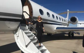 A woman in black descends from a private jet on a sunny day, embodying nonprofit leadership and advocacy.| Linda’s Life – Linda Smith