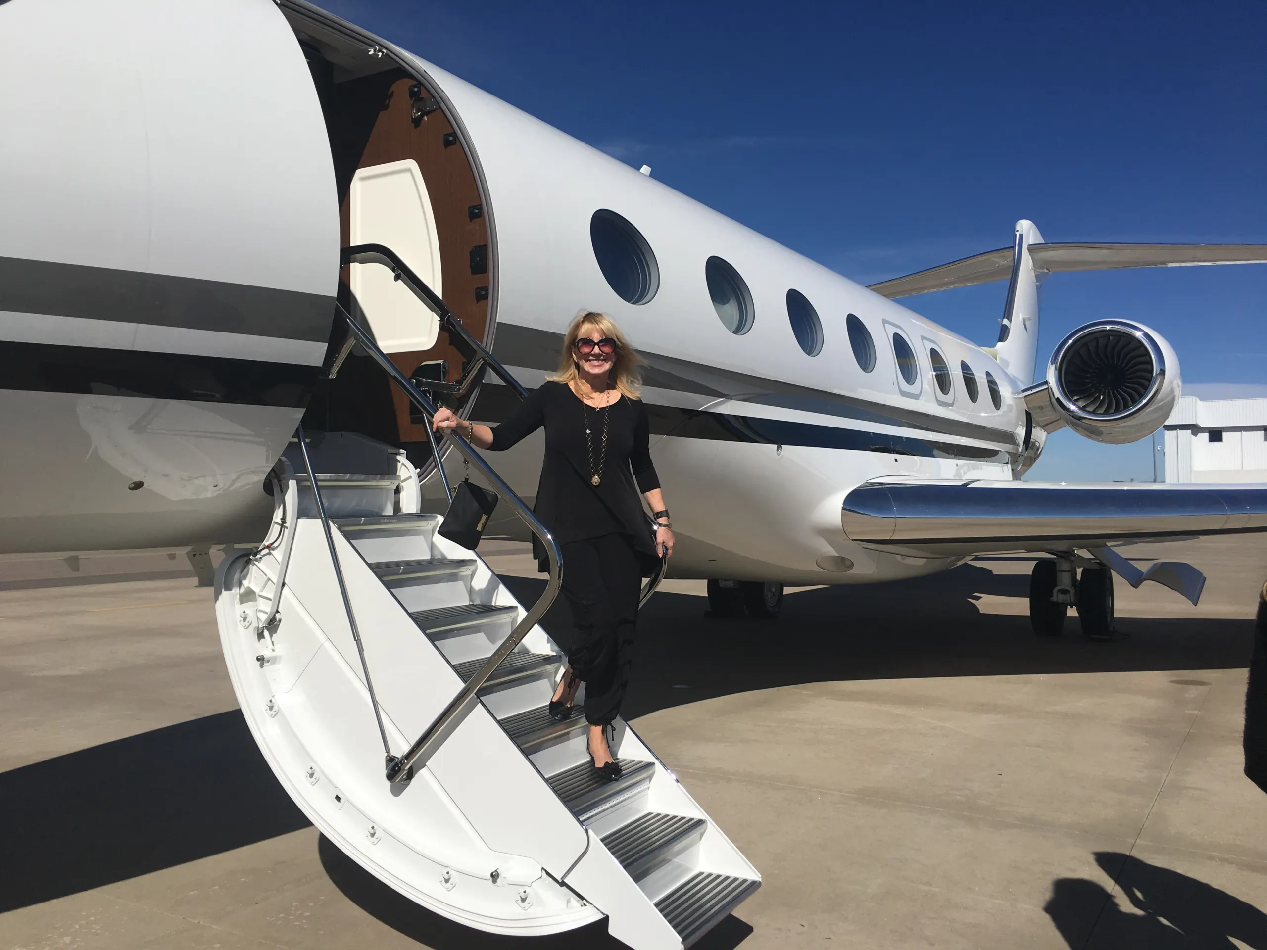 A woman in black descends from a private jet on a sunny day, embodying nonprofit leadership and advocacy.| Linda’s Life – Linda Smith