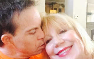 A woman smiles warmly as she receives a kiss on the cheek from a man, capturing a moment of personal connection and joy, reflecting themes of advocacy and inspirational storytelling relevant to Down syndrome awareness and disability advocacy.| Linda’s Life – Linda Smith