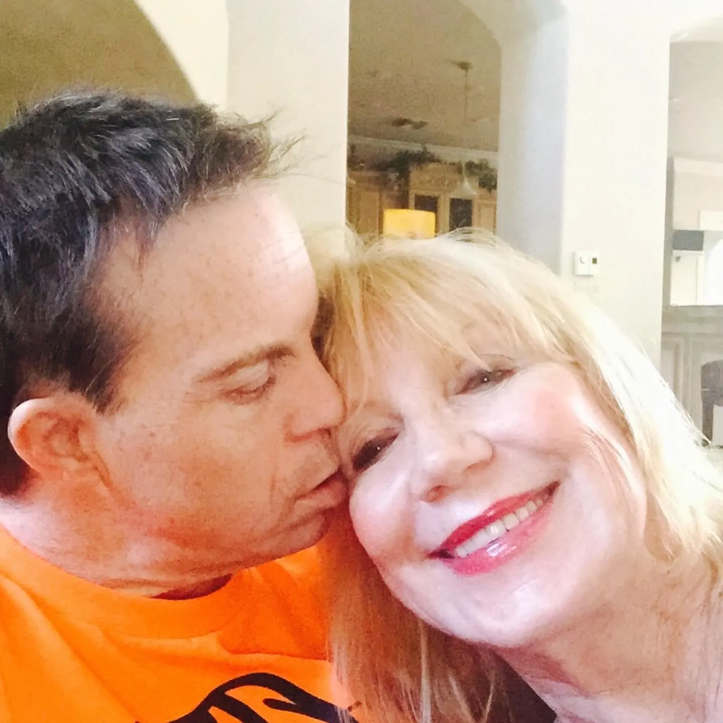 A woman smiles warmly as she receives a kiss on the cheek from a man, capturing a moment of personal connection and joy, reflecting themes of advocacy and inspirational storytelling relevant to Down syndrome awareness and disability advocacy.| Linda’s Life – Linda Smith
