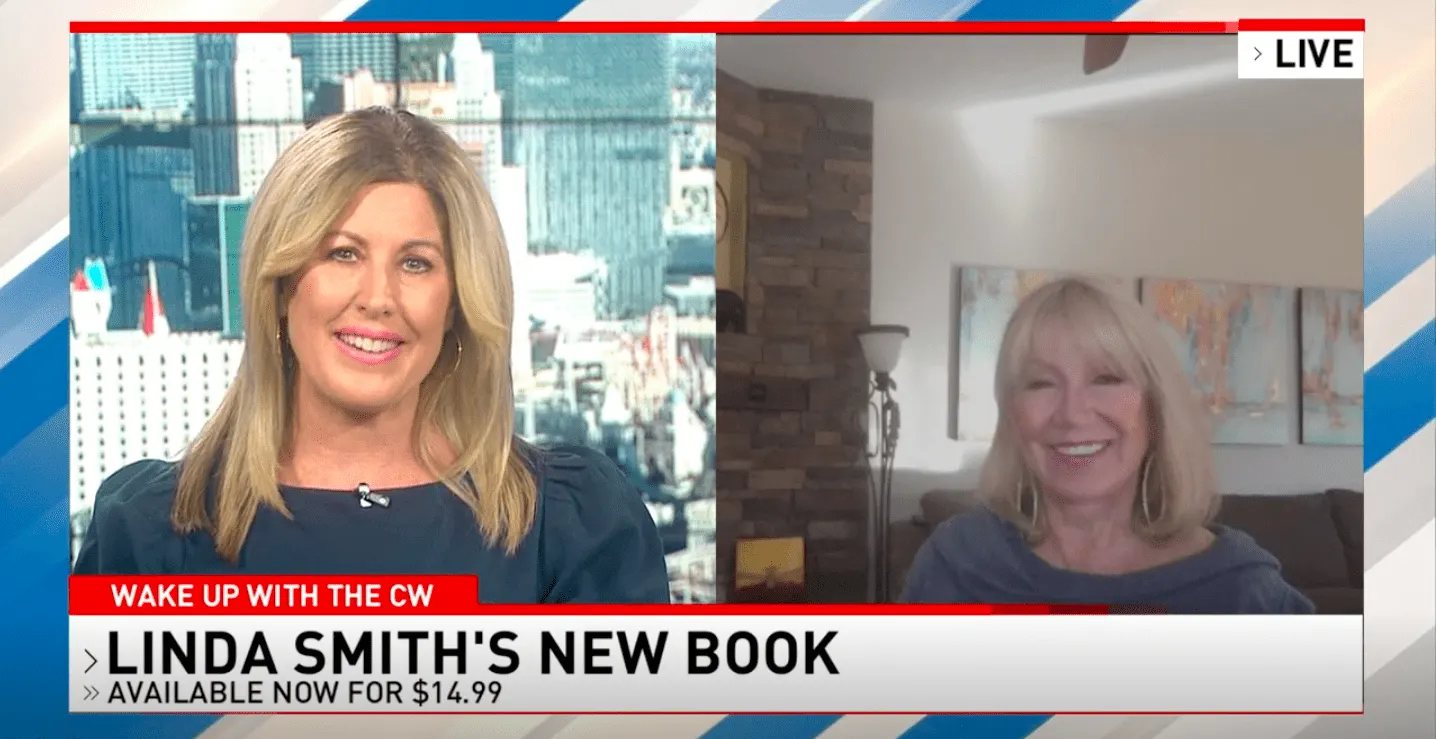 A smiling woman, a motivational speaker, is interviewed via video call. The TV screen displays "Linda Smith's New Book" with a price tag. Nearby, a cityscape is visible through a window.| Linda’s Life – Linda Smith
