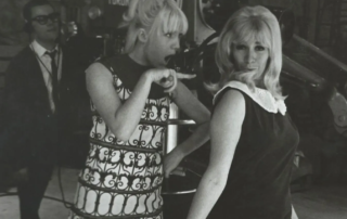 Two women in 1960s attire are in a TV studio, one pointing and speaking animatedly. A man with glasses stands behind them with equipment. This…| Linda’s Life – Linda Smith