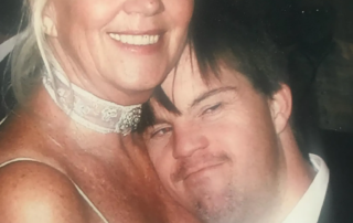 A smiling woman in a white dress hugs a young man in a suit, symbolizing Linda Smith's advocacy for Down syndrome awareness through inspirational storytelling and nonprofit leadership.| Linda’s Life – Linda Smith