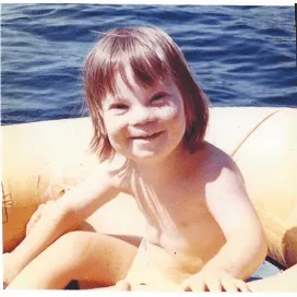 A young child with a joyful smile sits in a yellow inflatable boat on a sunny day, reflecting themes of innocence and happiness. This image connects to Linda Smith's advocacy for Down syndrome awareness and inspirational storytelling.| Linda’s Life – Linda Smith